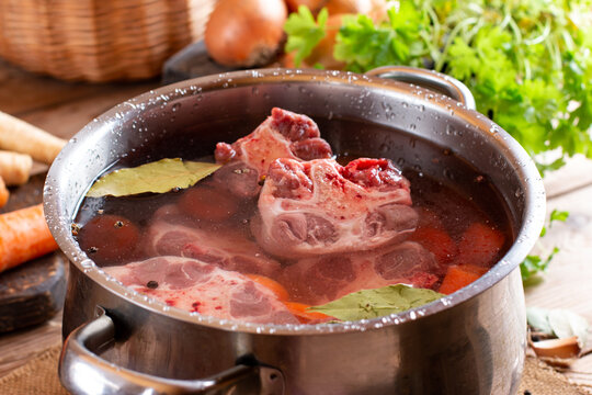 Raw veal beef Oxtail Meat with carrots, onions and spices in a saucepan on the table. Bone Broth Bouillon preparation Photos | Adobe Stock